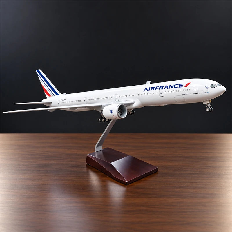 Air France Boeing 777-300ER 1:157 scale aircraft display model with LED cabin lighting, metal stand and wooden base, displayed on a living room table.
