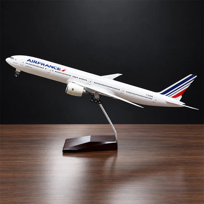Air France Boeing 777-300ER 1:157 scale aircraft display model with LED cabin lighting, metal stand and wooden base, displayed on a living room table.