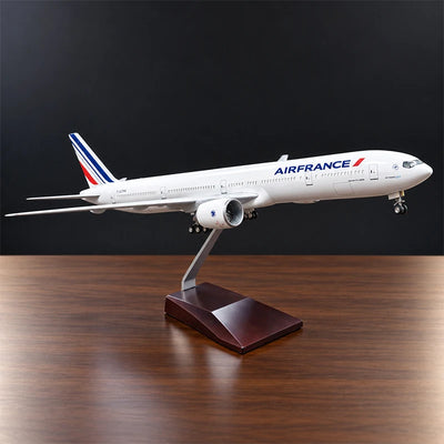 Air France Boeing 777-300ER 1:157 scale aircraft display model with LED cabin lighting, metal stand and wooden base, displayed on a living room table.